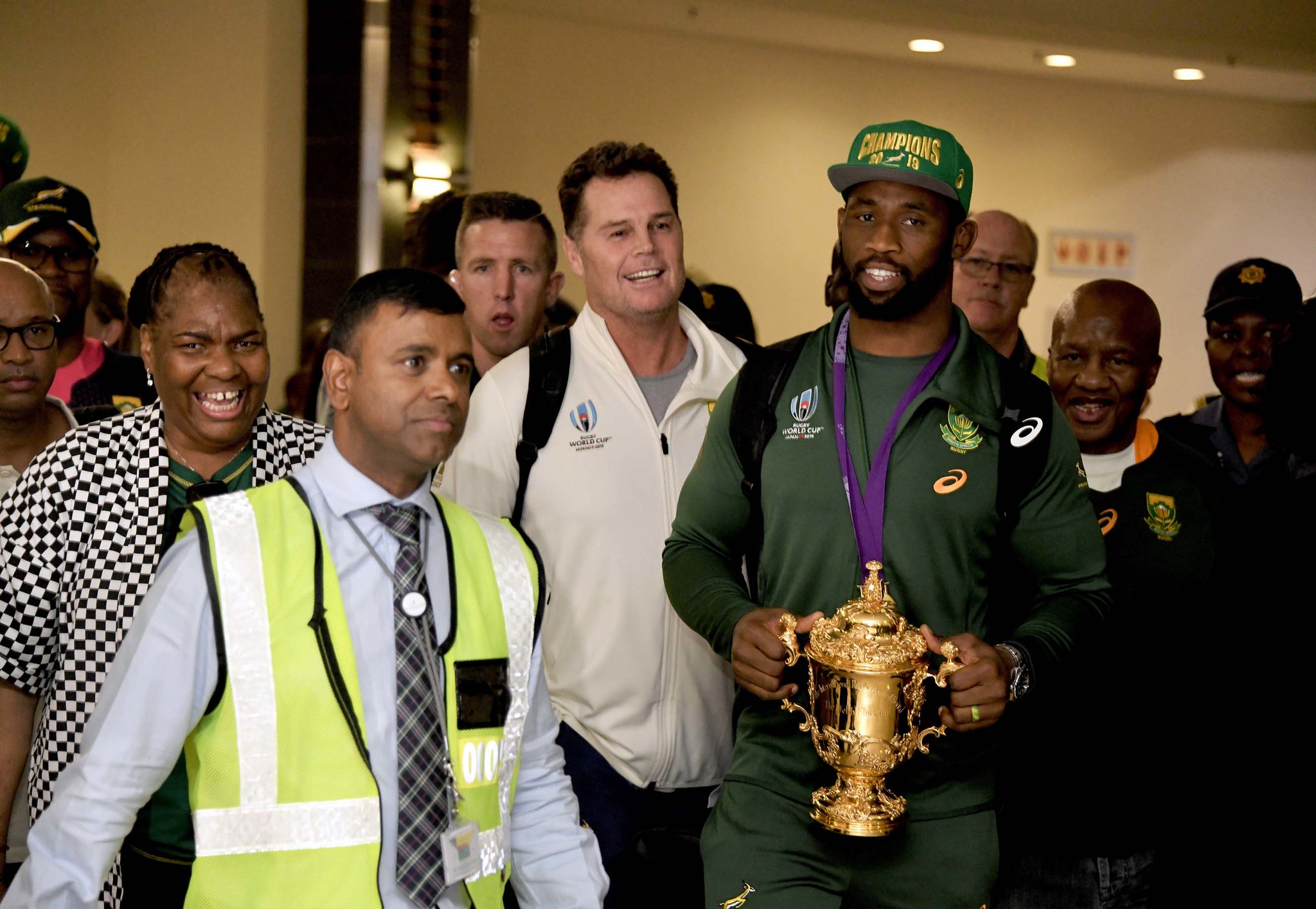 Springboks Captain, Siya Kolisi, walking through a crowd holding the Webb Ellis trophy.