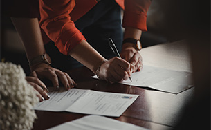 Two individuals signing legal documents at a table, symbolizing a formal agreement or contract