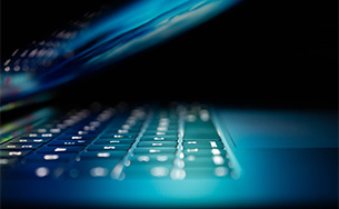 Half closed laptop in a dark room and screen illuminating the keyboard