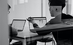 Two people working on their laptops at a table discussing a project