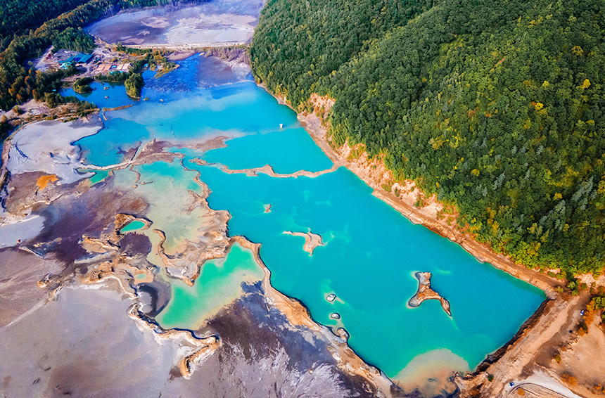 Blue waters of a former tailings dam next to green forest